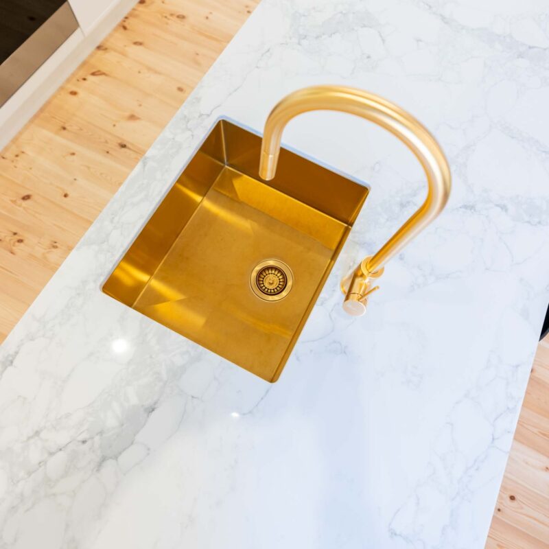 Brushed gold goose neck mixer tap and undermount sink. large light marble island benchtop.