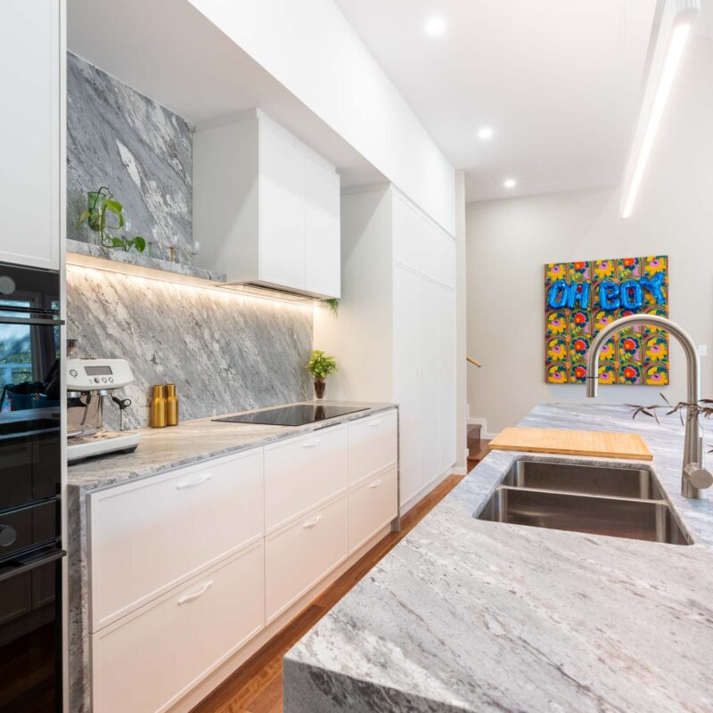 Modern kitchen with large island benchtop. White thin shaker profiled cabinets with a bold grey marble benchtop and splashback.