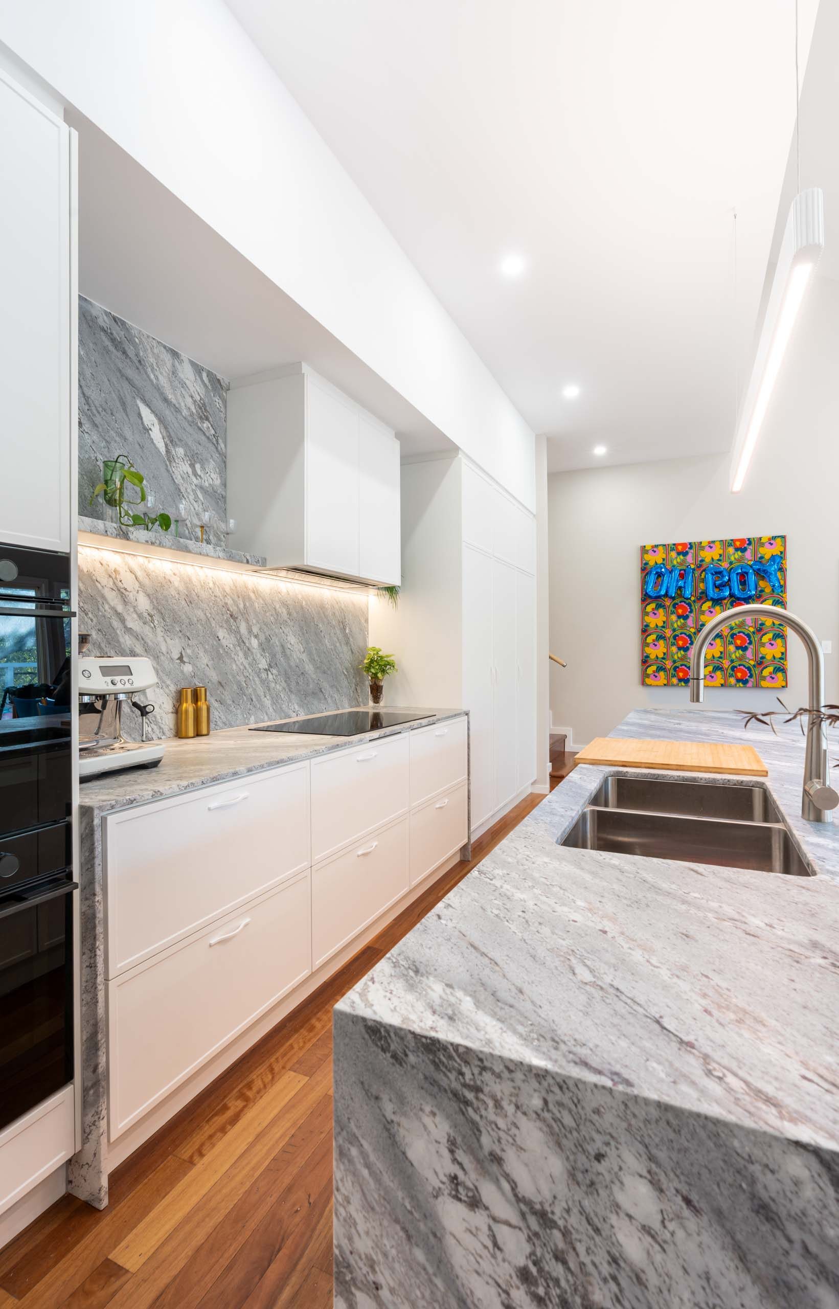 Modern kitchen with large island benchtop. White thin shaker profiled cabinets with a bold grey marble benchtop and splashback.