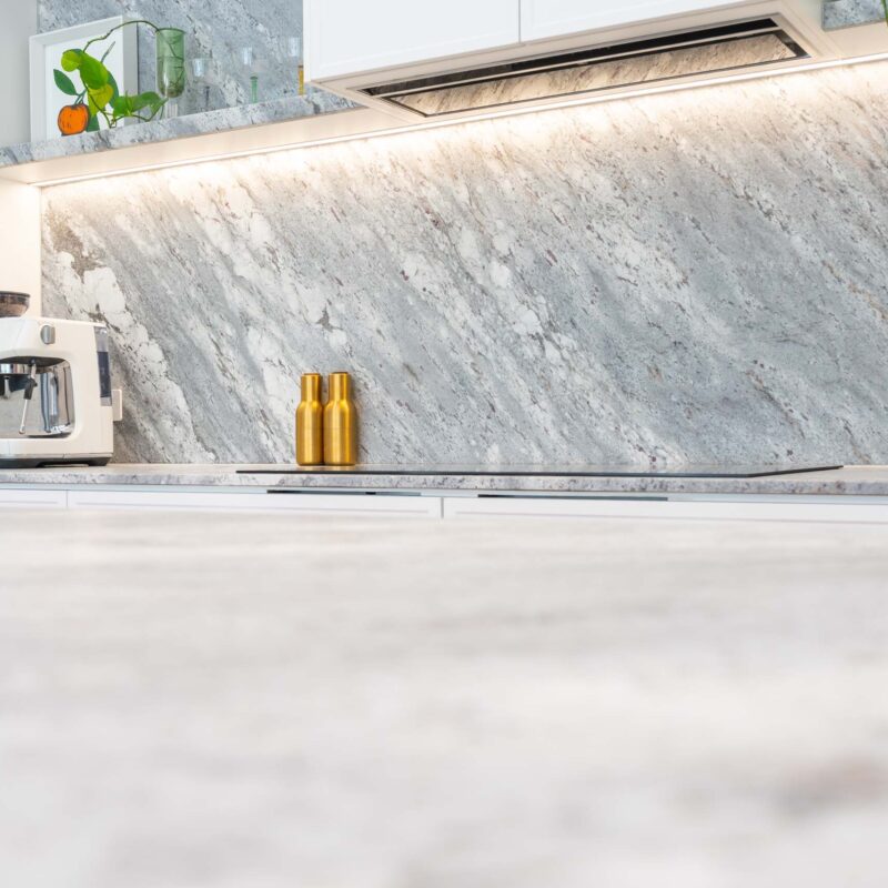 Bold grey marble splash back featuring matching floating shelves either side of a white range hood cabinet.