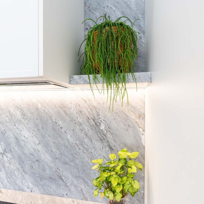 Grey marble floating shelf beside a white overhead cabinet concealing a built in rangehood.