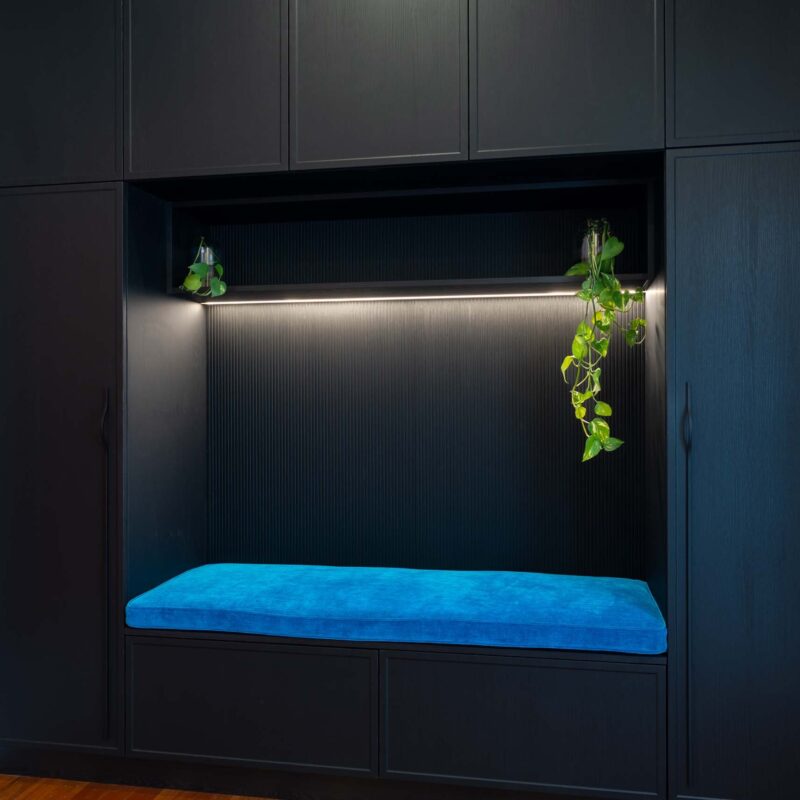 Large built-in bench seat with storage above and below, framed by floor-to-ceiling cabinetry on either side. Includes an open shelf above the bench seat and black woodgrain cabinet doors and drawers.