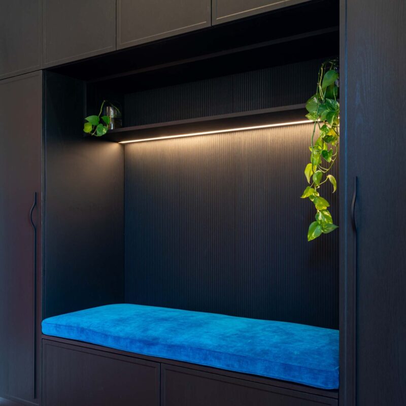 Large built-in bench seat with storage above and below, framed by floor-to-ceiling cabinetry on either side. Includes an open shelf above the bench seat and black woodgrain cabinet doors and drawers.