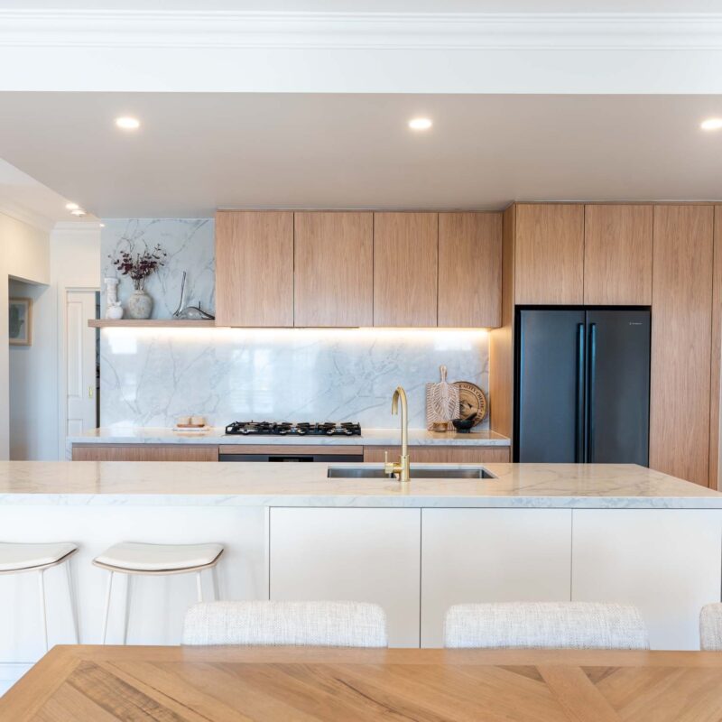 A modern classic kitchen with a large island benchtop. Featuring a mixture of oak timber look and white laminate finger pull cabinets with light marble benchtops.