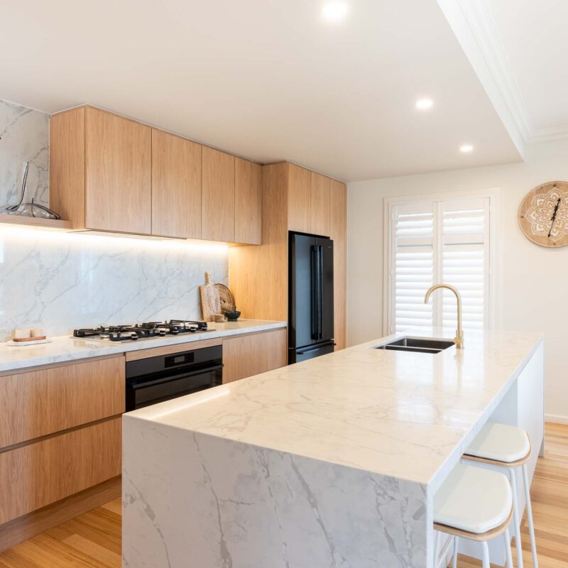 A modern classic kitchen with a large island benchtop. Featuring a mixture of oak timber look and white laminate finger pull cabinets with light marble benchtops.