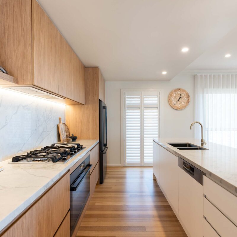 A modern classic kitchen with a large island benchtop. Featuring a mixture of oak timber and white laminate finger pull cabinets and light marble benchtops with waterfall ends.