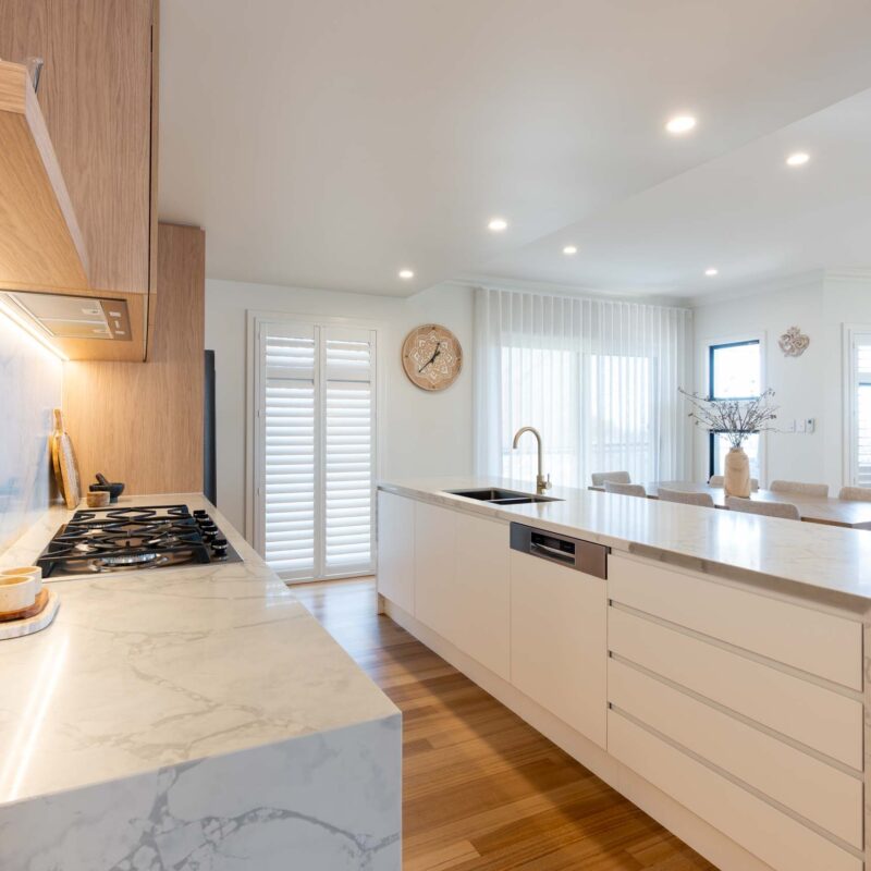 A modern classic kitchen with a large island benchtop. Featuring a mixture of oak timber look and white laminate finger pull cabinets with light marble benchtops.