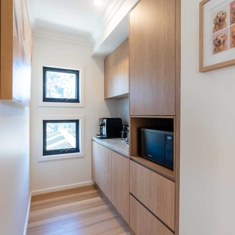 Butlers pantry featuring timber laminate finger pull cabinets and light marble benchtops and matching splashback.