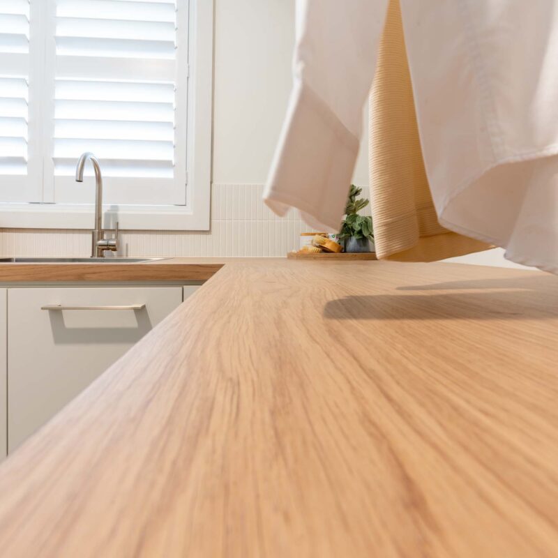 Laundry with timber look laminate benchtops and white matte cabinets.