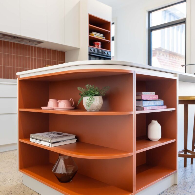 Island bench cabinetry featuring burnt orange laminate open shelf display cabinets and a thin white engineered stone benchtop.