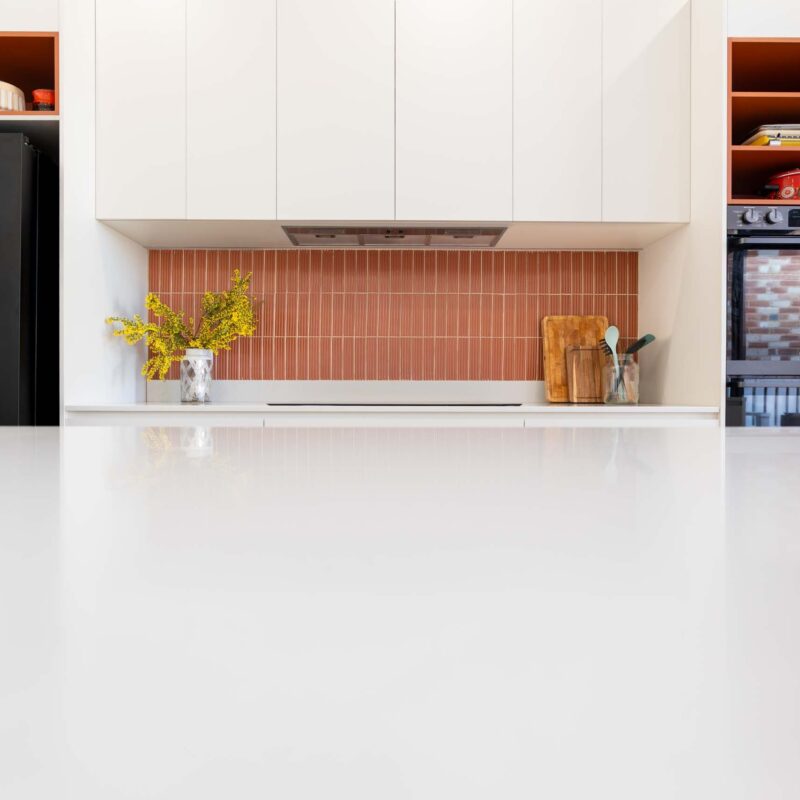 Matte white kitchen with a mix of burnt orange laminate open shelving and a matching fluted orange tiled splashback.