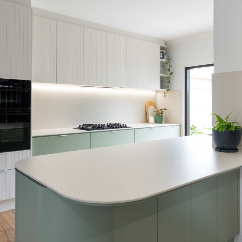 A fresh two toned galley style kitchen featuring matte green base cabinets and slatted style matte white overhead cabinets. Includes white engineered stone benchtops with curved edges. Matt white lip pull handles.