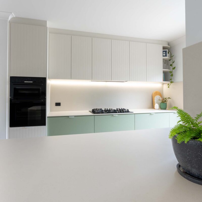 A fresh two toned galley style kitchen featuring matte green base cabinets and slatted style matte white overhead cabinets. Includes white engineered stone benchtops and white lip handles.