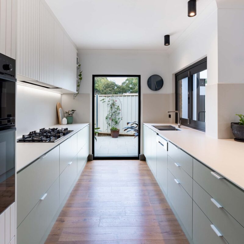 A fresh two toned galley style kitchen featuring matte green base cabinets and slatted style matte white overhead cabinets. Includes white engineered stone benchtops and white lip handles.