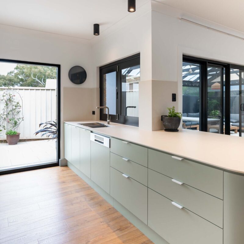 A fresh two toned galley style kitchen featuring matte green base cabinets and slatted style matte white overhead cabinets. Includes white engineered stone benchtops with curved edges. Matt white lip pull handles.
