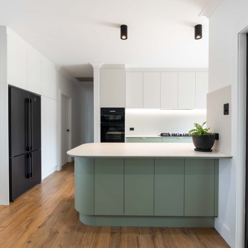 A fresh two toned galley style kitchen featuring matte green base cabinets and slatted style matte white overhead cabinets. Includes white engineered stone benchtops with curved edges.