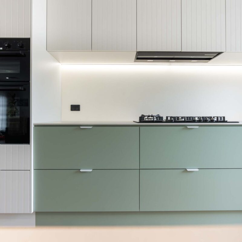 A fresh two toned galley style kitchen featuring matte green base cabinets and slatted style matte white overhead cabinets. Includes white engineered stone benchtops and white lip handles.