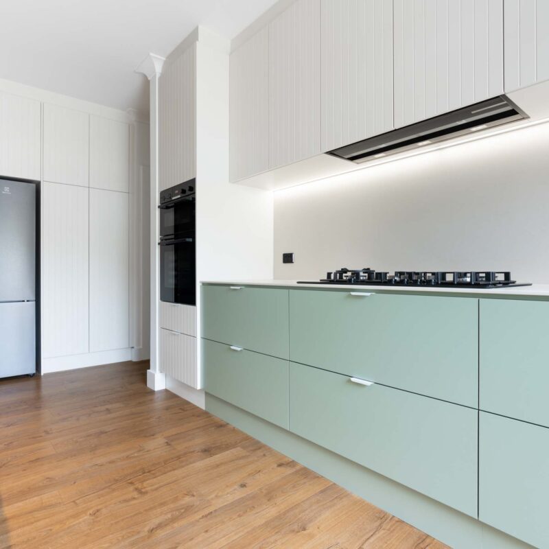 A fresh two toned galley style kitchen featuring matte green base cabinets and slatted style matte white overhead cabinets. Includes white engineered stone benchtops and white lip handles.
