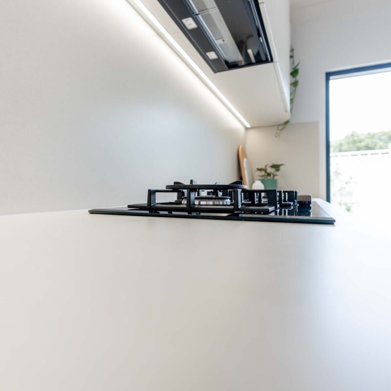 Gas cooktop installed into a white engineered stone benchtop. Indergrated rangehood above.