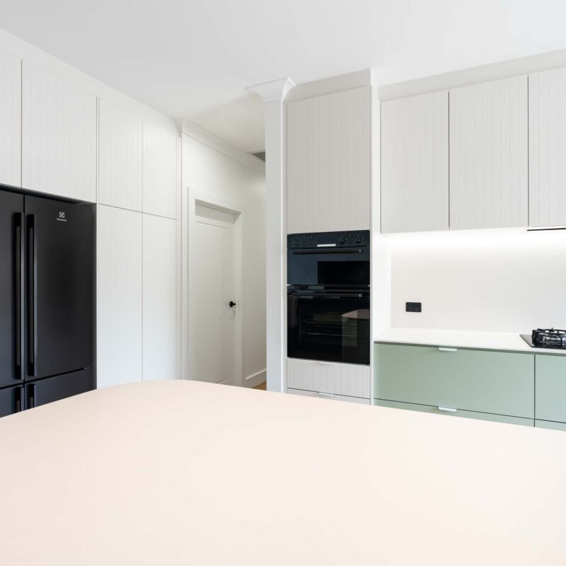 A fresh two toned galley style kitchen featuring matte green base cabinets and slatted style matte white overhead cabinets. Includes white engineered stone benchtops and white lip handles.