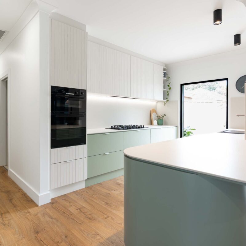 A fresh two toned galley style kitchen featuring matte green base cabinets and slatted style matte white overhead cabinets. Includes white engineered stone benchtops with curved edges.