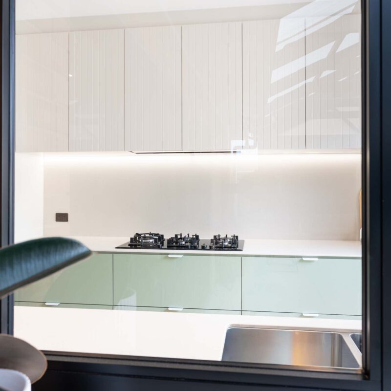 Looking through the kitchen window into a two tone kitchen featuring green base cabinet and slatted white overhead cabinets.