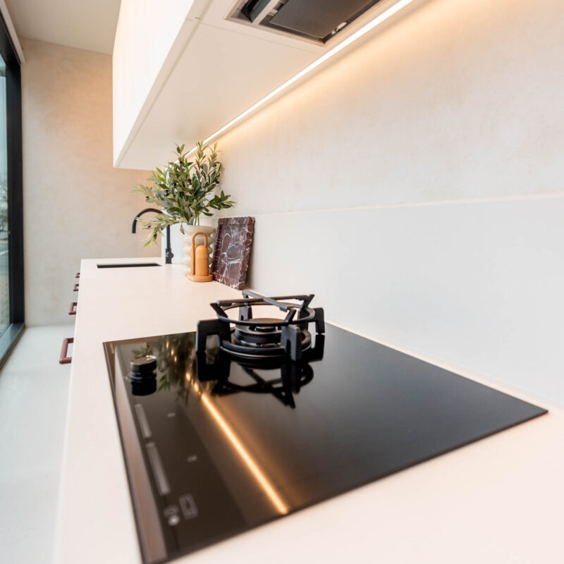 Small galley kitchen featuring a glass cooktop with 1 x gas trivet. Showcasing white benchtops and overhead cabinets with a integrated rangehood.