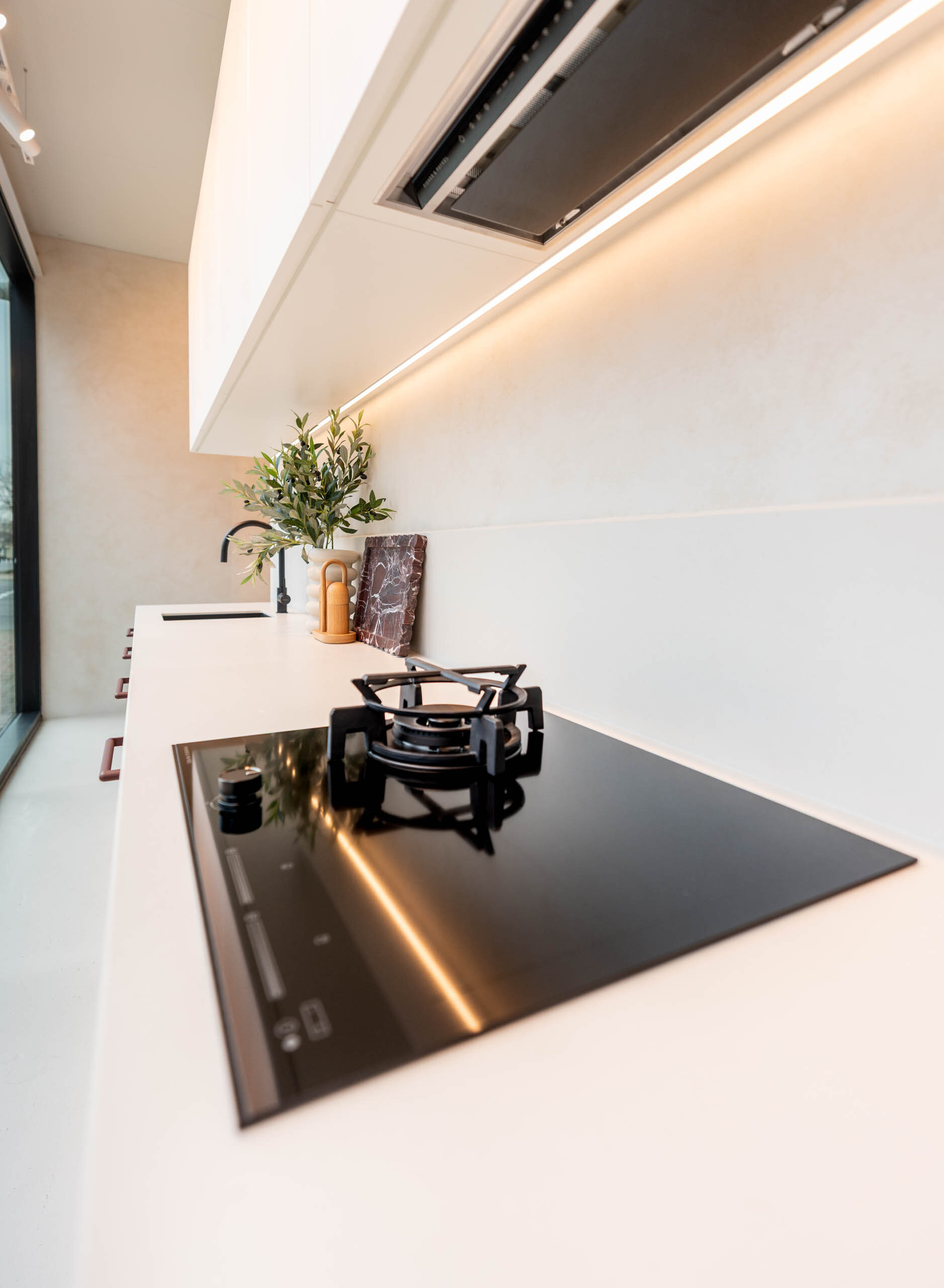 Small galley kitchen featuring a glass cooktop with 1 x gas trivet. Showcasing white benchtops and overhead cabinets with a integrated rangehood.