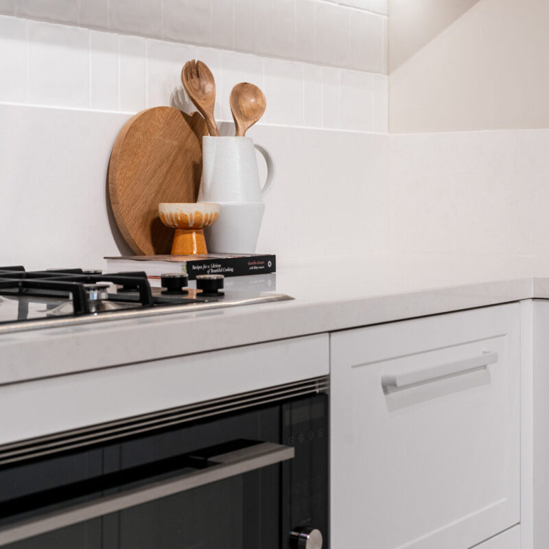Classic Hampton style kitchen featuring shaker style cabinets, a white engineered stone and floating timber shelving.