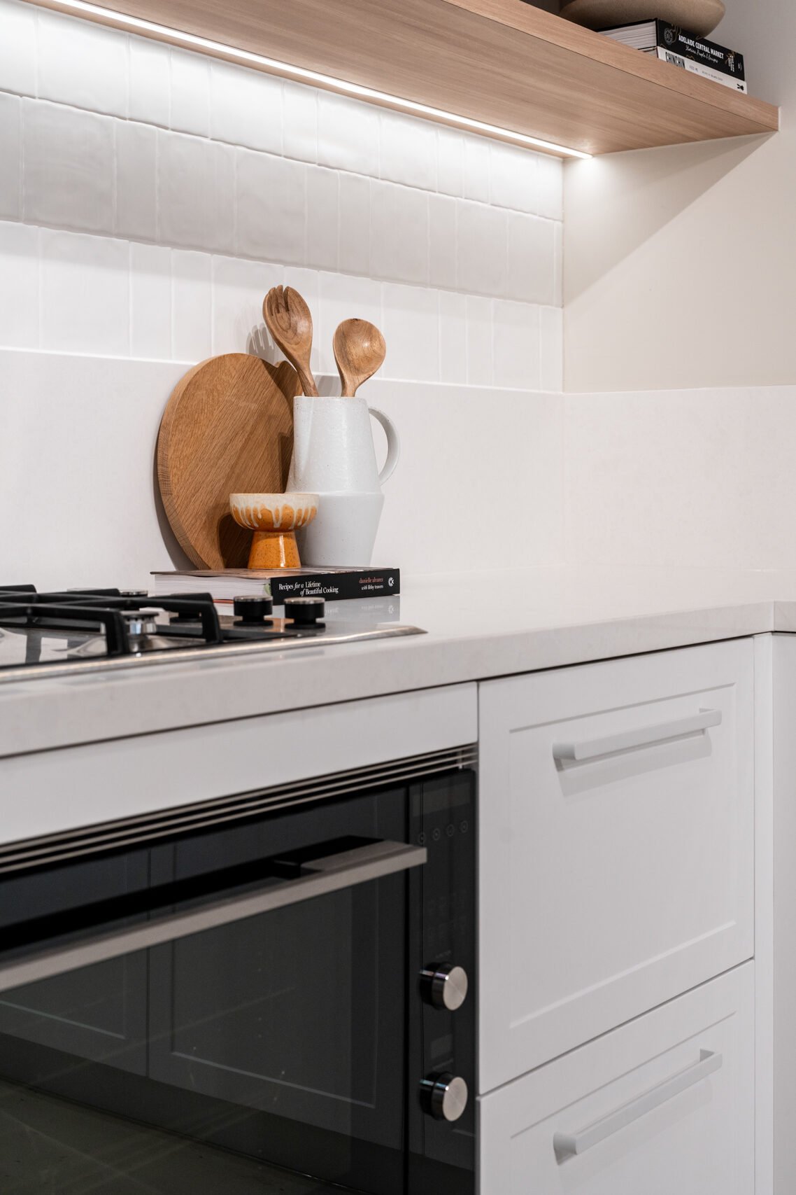 Classic Hampton style kitchen featuring shaker style cabinets, a white engineered stone and floating timber shelving.