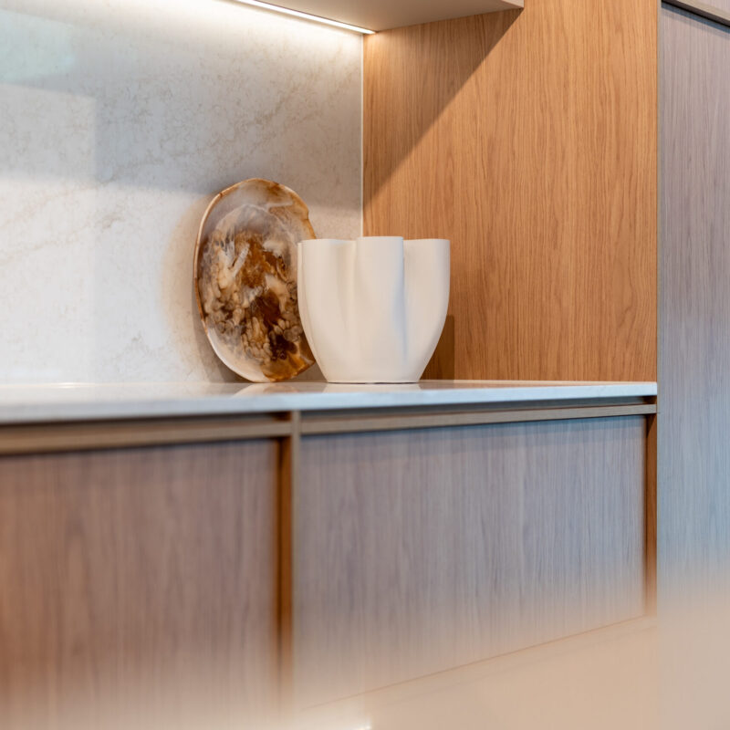 Modern kitchen featuring timber grain cabinets with a light organic stone benchtop.
