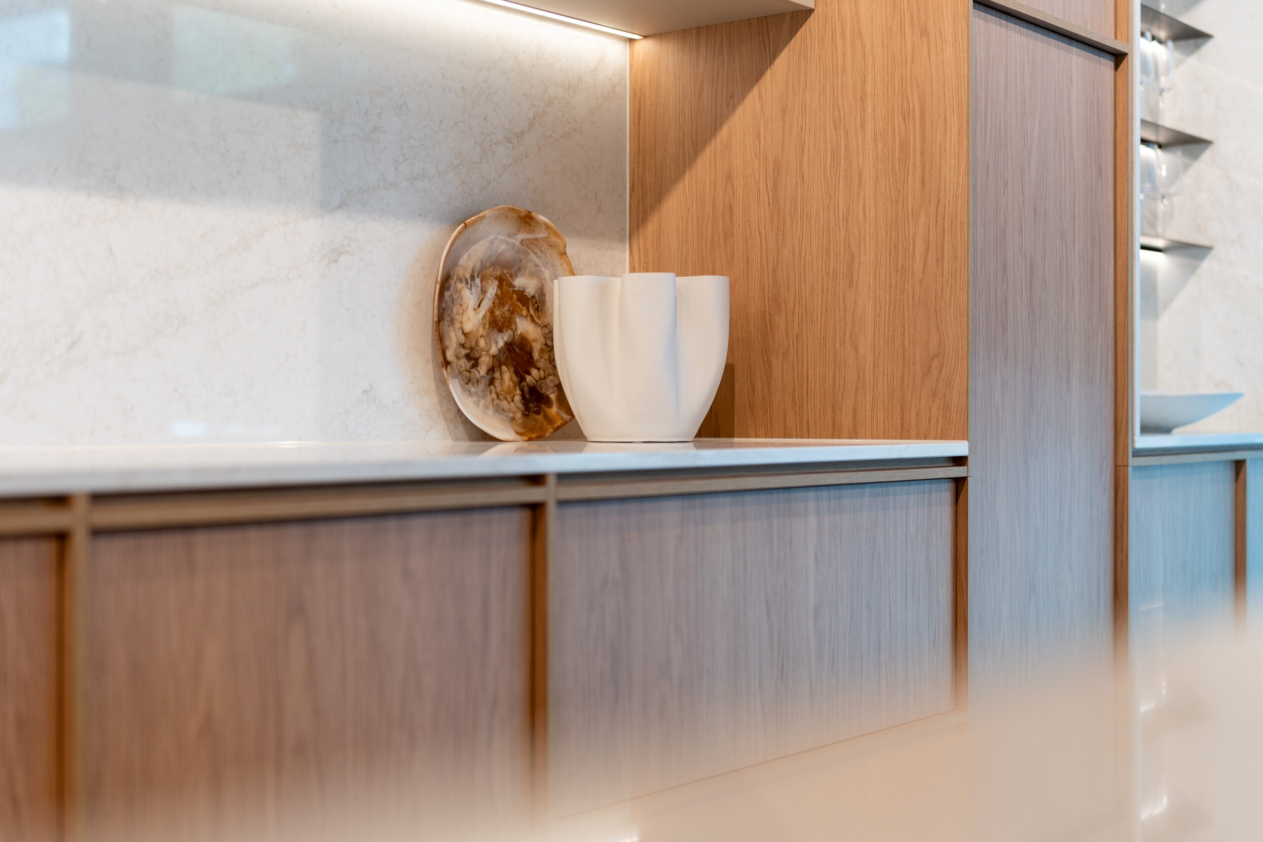Modern kitchen featuring timber grain cabinets with a light organic stone benchtop.