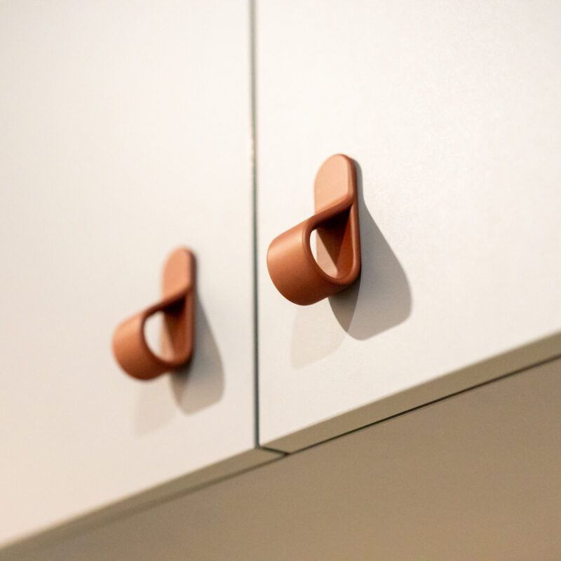 Light coloured kitchen cabinets featuring small terracotta coloured curved handles.