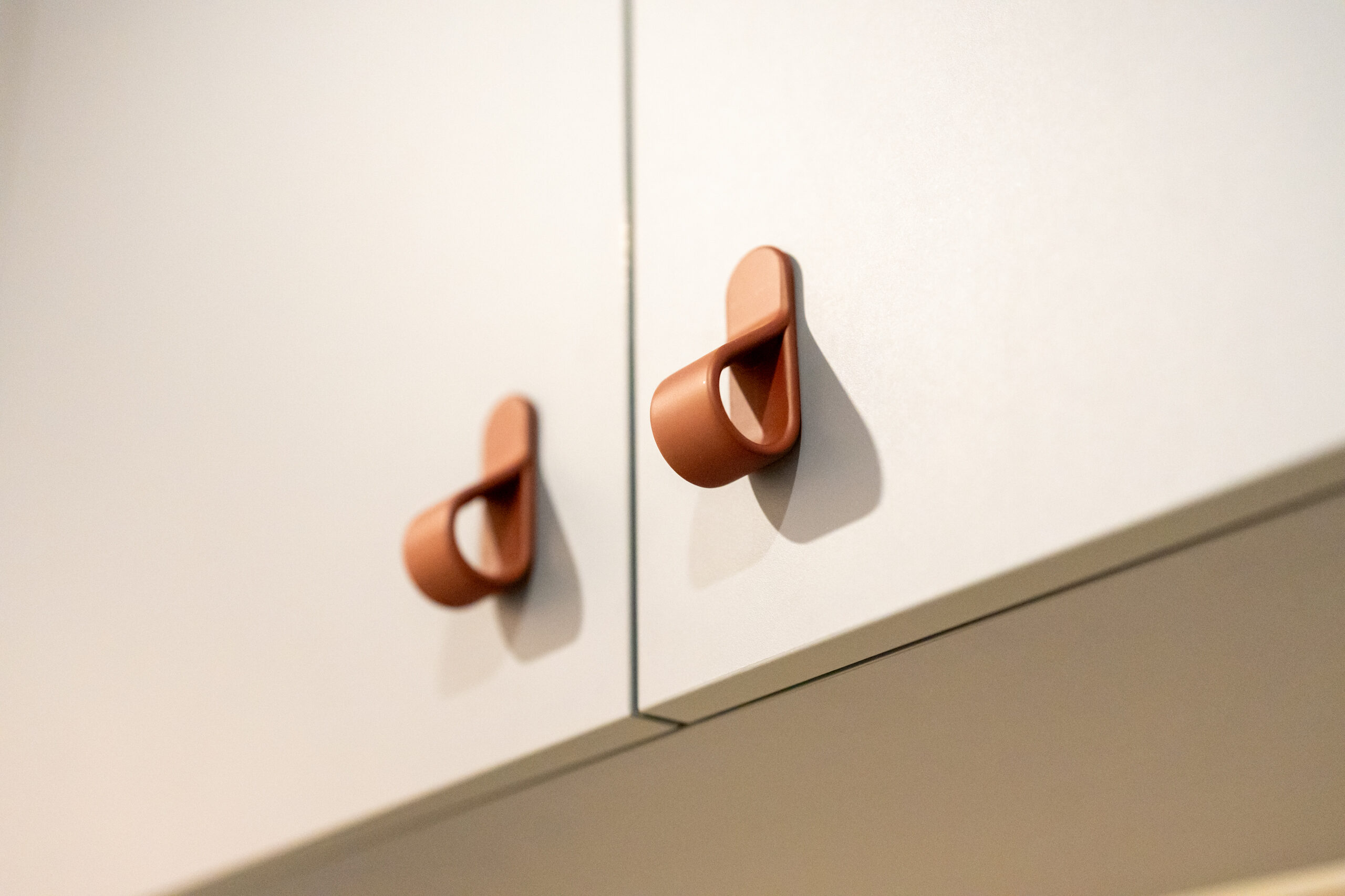 Light coloured kitchen cabinets featuring small terracotta coloured curved handles.