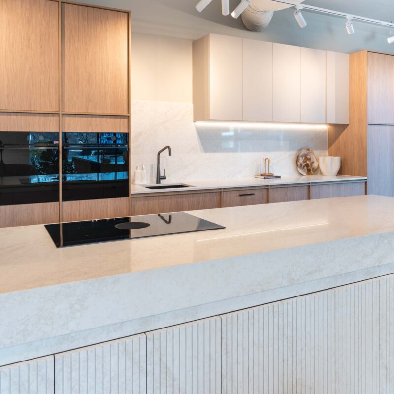 Modern two tone kitchen featuring timber grain and white cabinets with a light organic stone benchtop with fluted stone hidden cabinets in the island.