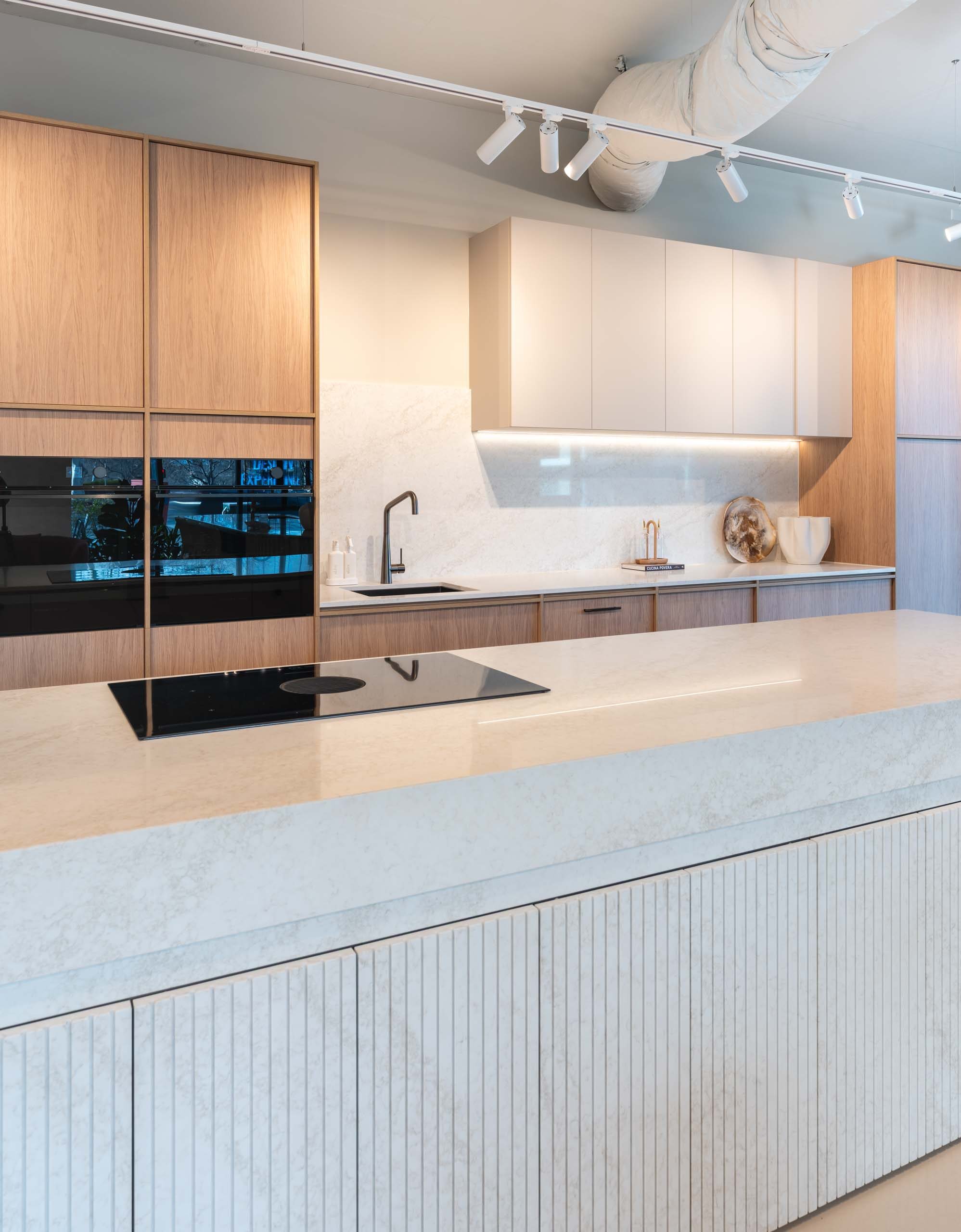 Modern two tone kitchen featuring timber grain and white cabinets with a light organic stone benchtop with fluted stone hidden cabinets in the island.