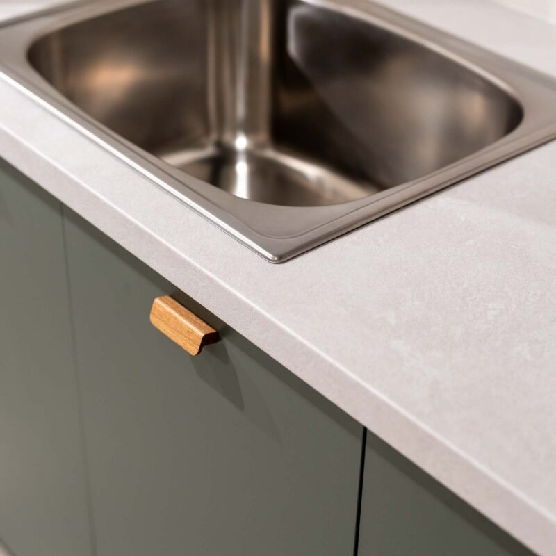 Laundry display featuring matte green cabinets with small timber handles. A light laminate benchtop.
