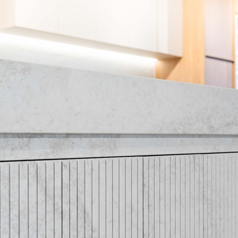 Modern kitchen island featuring hidden cabinets made from vertical fluted grooved stone doors.