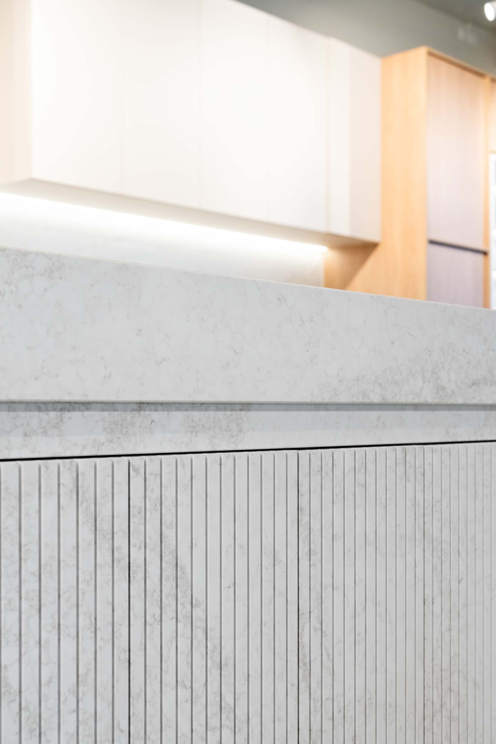 Modern kitchen island featuring hidden cabinets made from vertical fluted grooved stone doors.