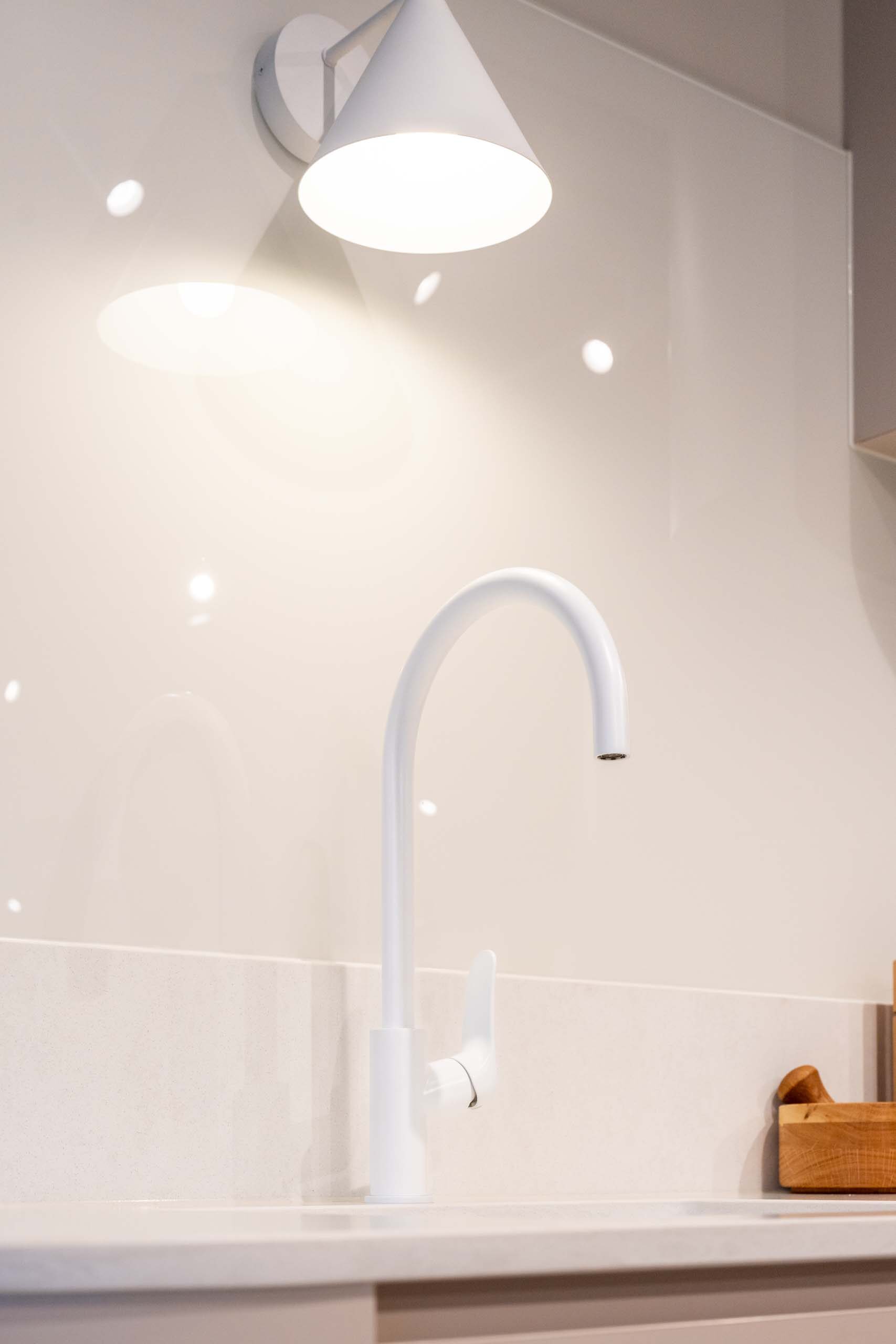 White goose neck mixer tap. Solid surface combined with a glass splash back.