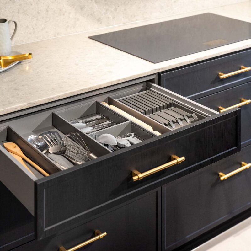 Dark timber grain kitchen with light solid surface benchtops, showing the internal drawer dividers creating an organised cutlery drawer.
