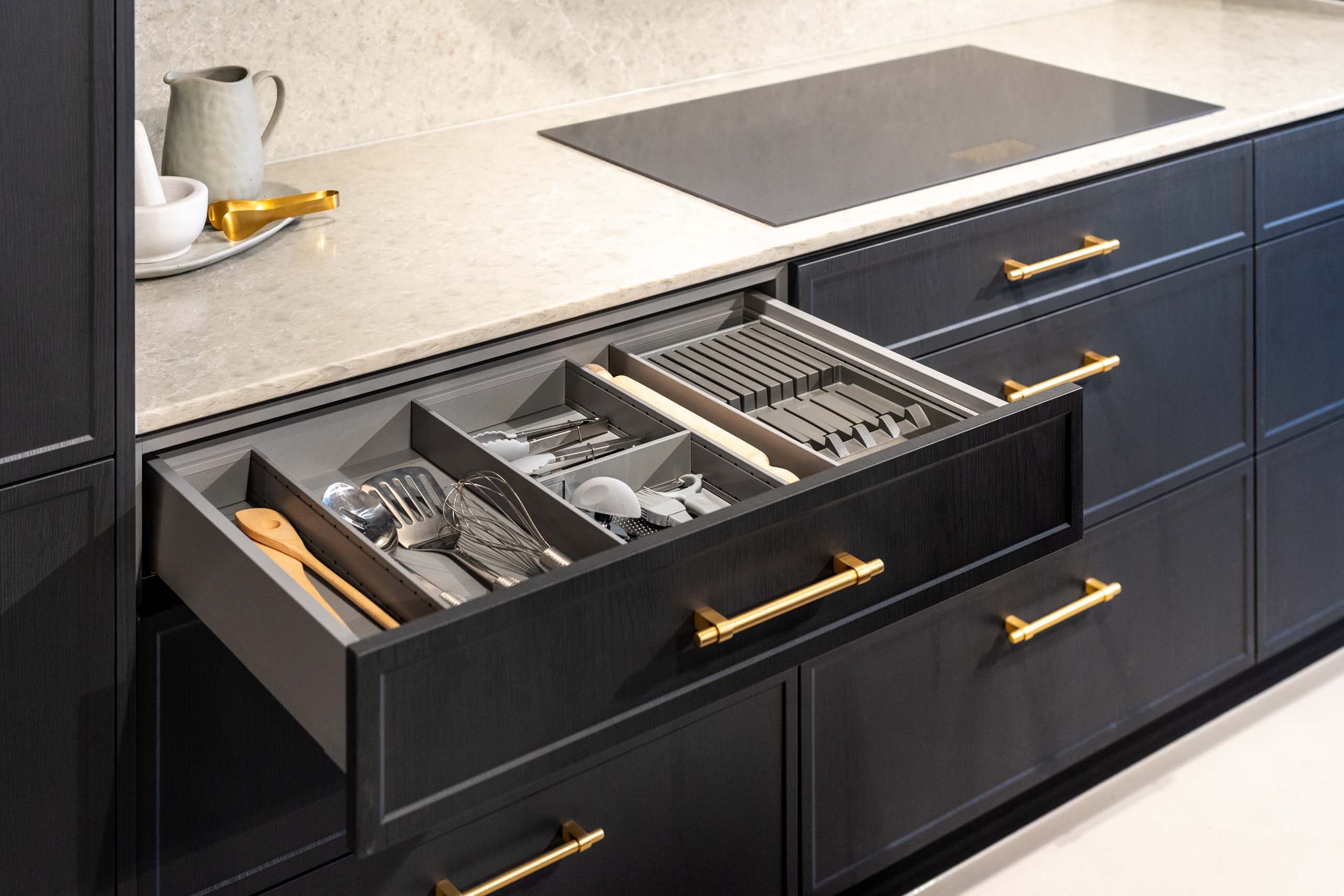 Dark timber grain kitchen with light solid surface benchtops, showing the internal drawer dividers creating an organised cutlery drawer.
